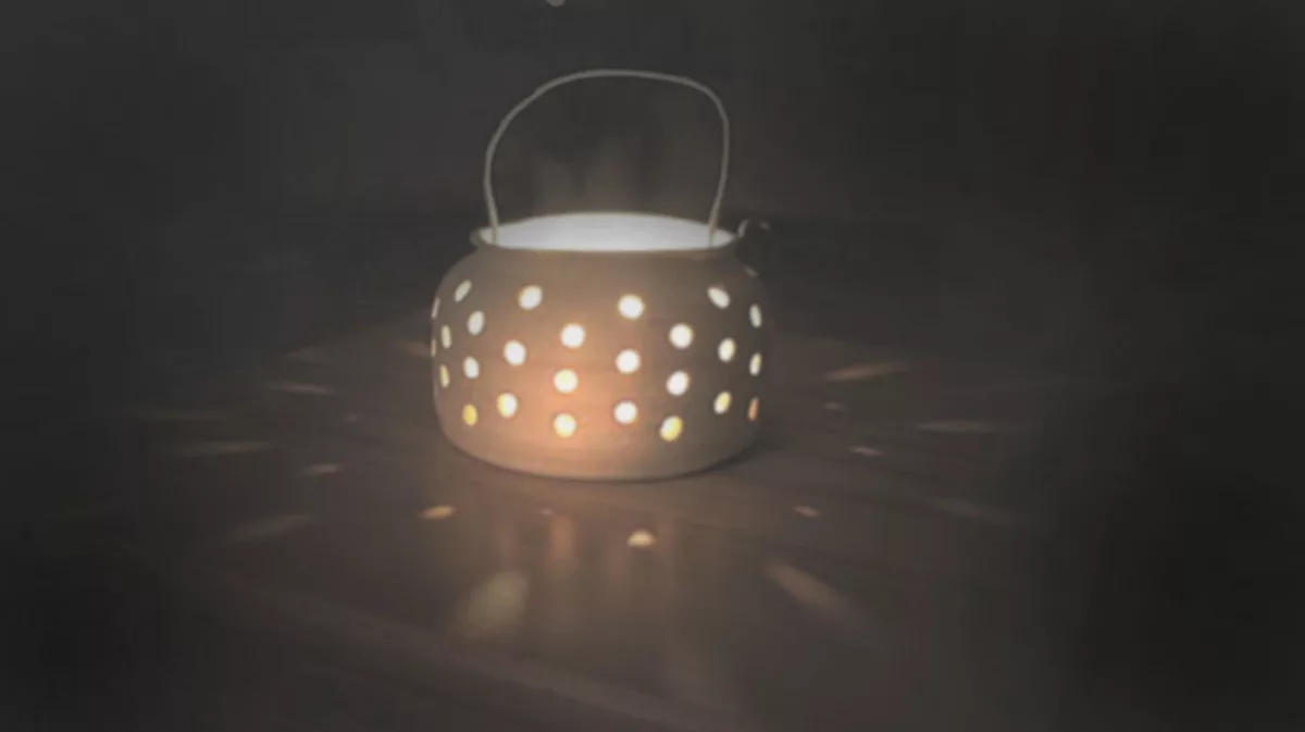 Candle pot with a wire handle, lit